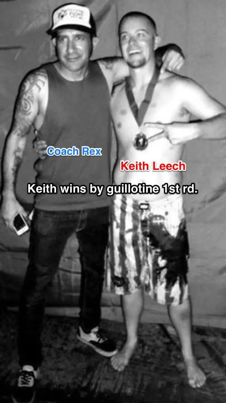 Keith Leech pointing at his winner's medal with Coach Rex's arm around him backstage