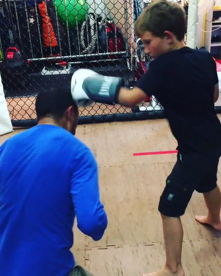 A young student throwing a straight right into a coach's focus mitt beside the cage