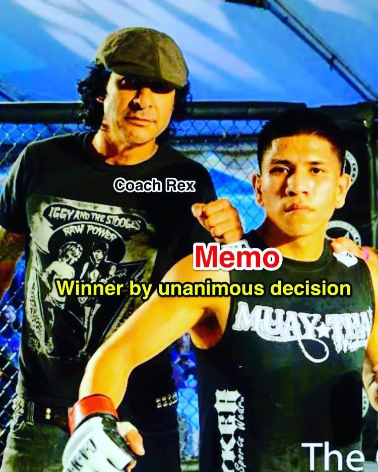 Coach Rex in a flat cap beside fighter Memo, gloved fist raised on fight night