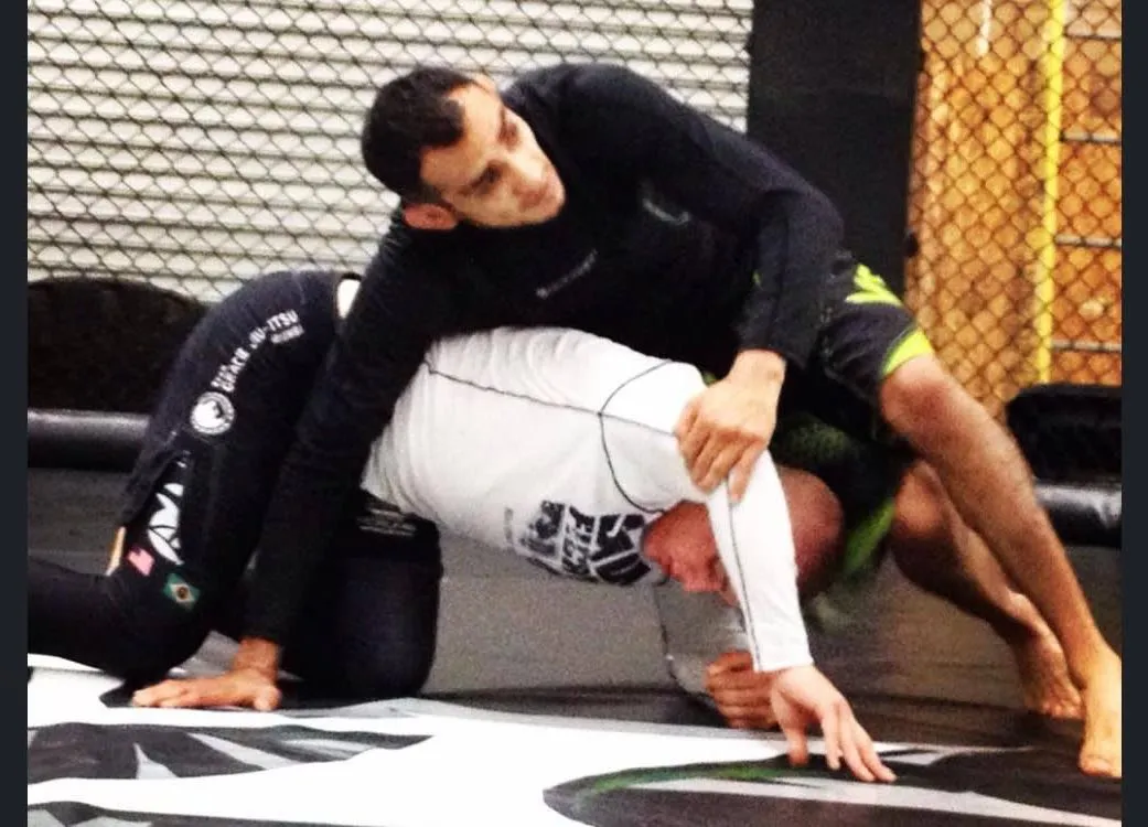 No-gi grappler in a black rash guard passing his partner's guard on the cage mat