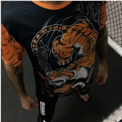Navy Venum tee with an orange tiger and Thai script, worn beside the cage