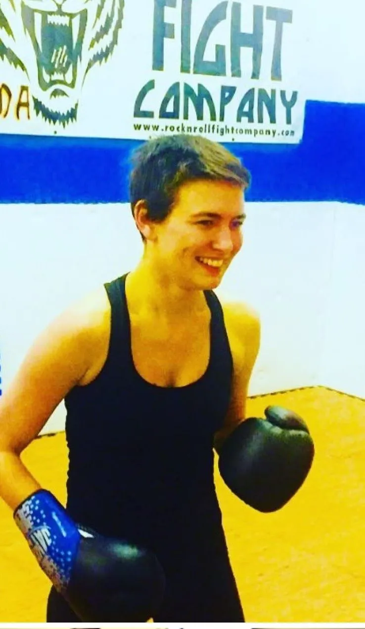 A student smiling in boxing gloves under the tiger-head Rock N Roll Fight Company banner
